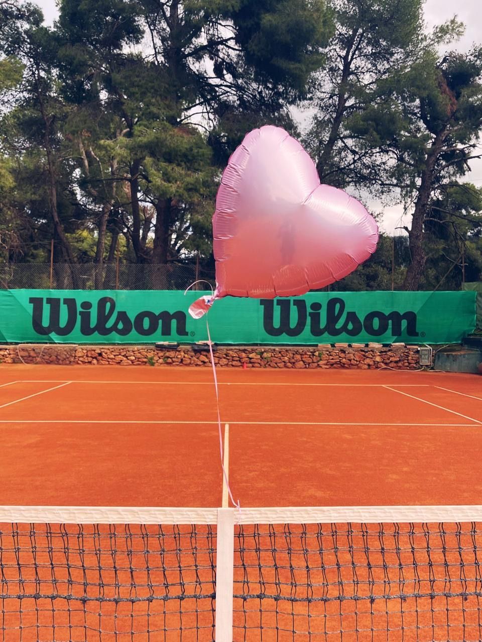 Heart balloon on the clay, Wilson banners and pines behind